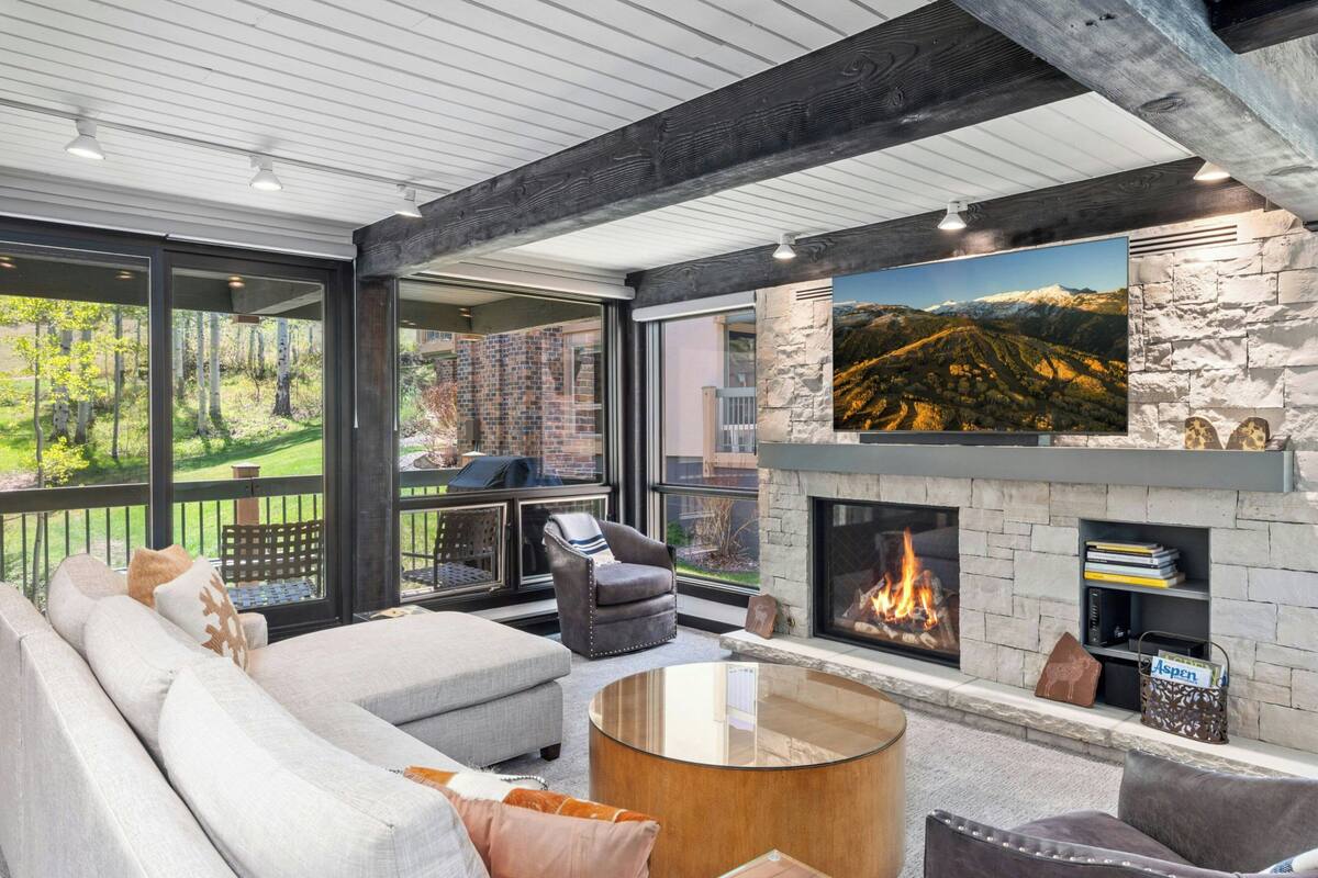 A modern living room with a fireplace, large windows, and a stone accent wall.