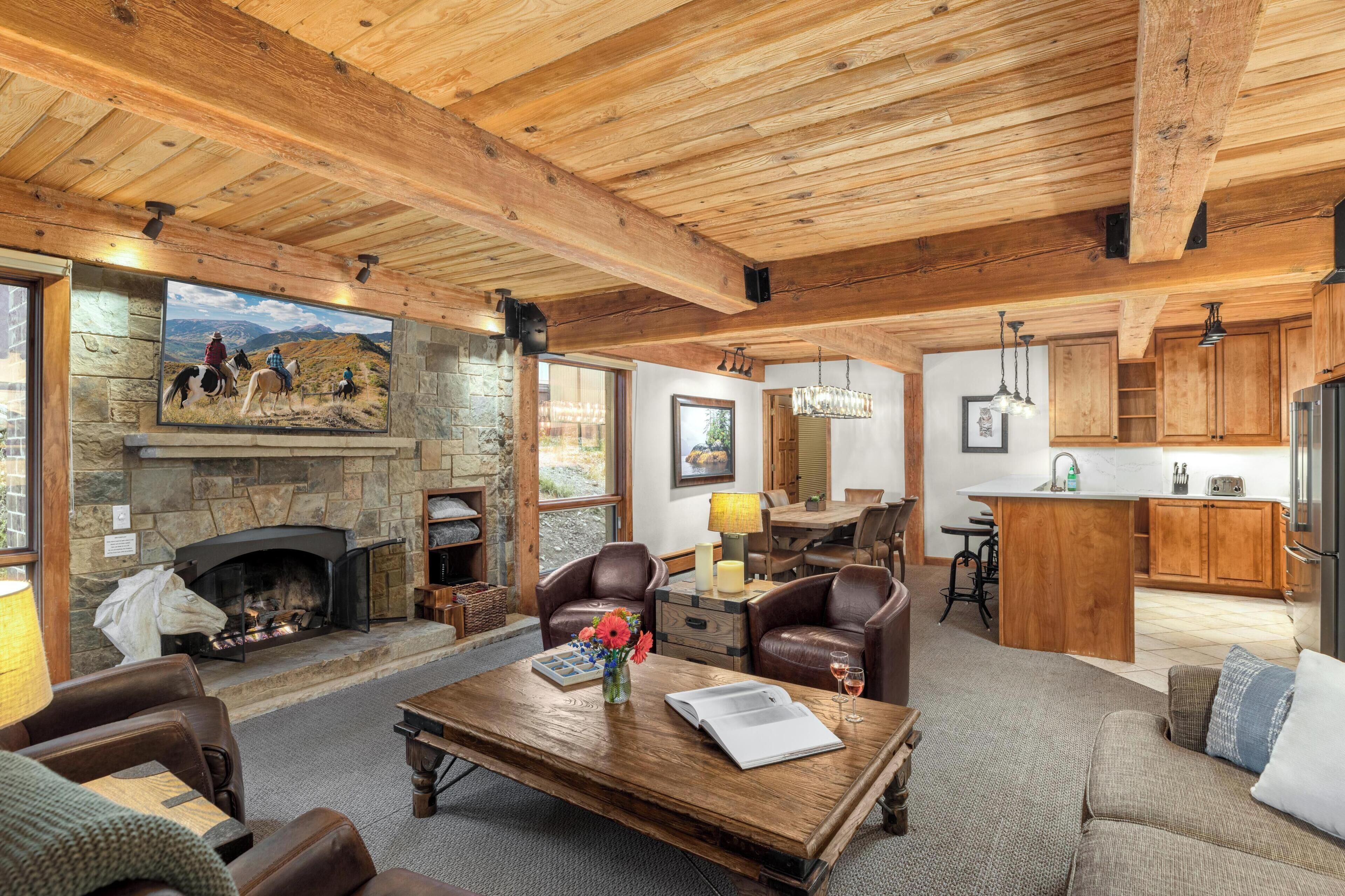 A spacious living room with a stone fireplace, leather furniture, and a large window overlooking a scenic landscape.