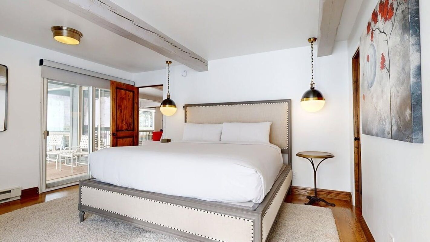 A bedroom with a large bed, a sliding glass door to a balcony, and a painting on the wall.
