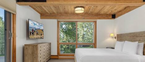 Ein Schlafzimmer mit Holzboden, einem großen Fenster, einem Bett, einem Schminktisch und einem Gemälde an der Wand.