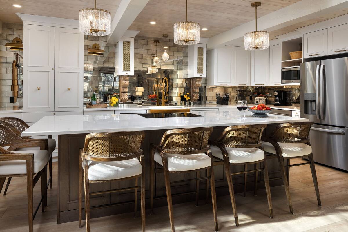 A modern kitchen with a large island, bar stools, stainless steel appliances, and decorative lighting.