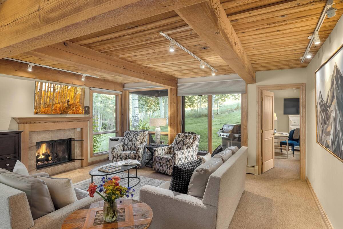 A spacious living room with a fireplace, comfortable seating, and large windows offering a view of the outdoors.