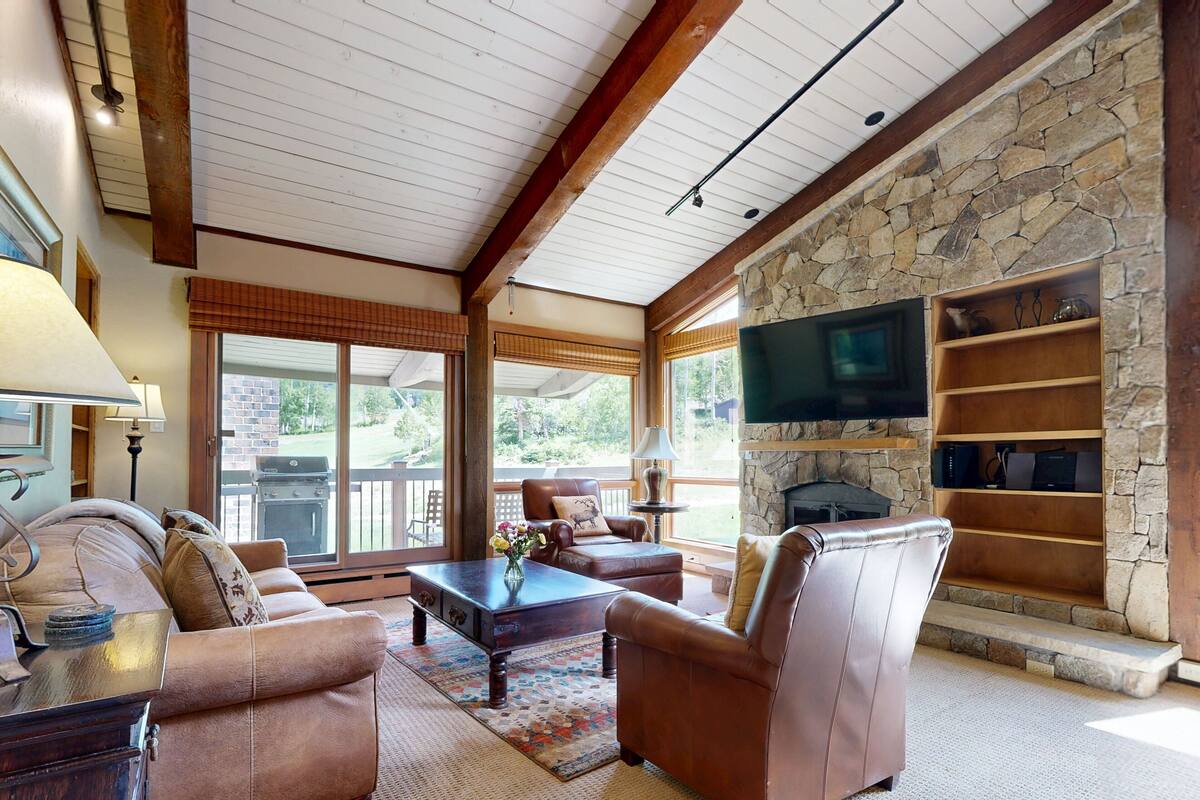 A spacious living room with leather sofas, a stone fireplace, and a television mounted on the wall.