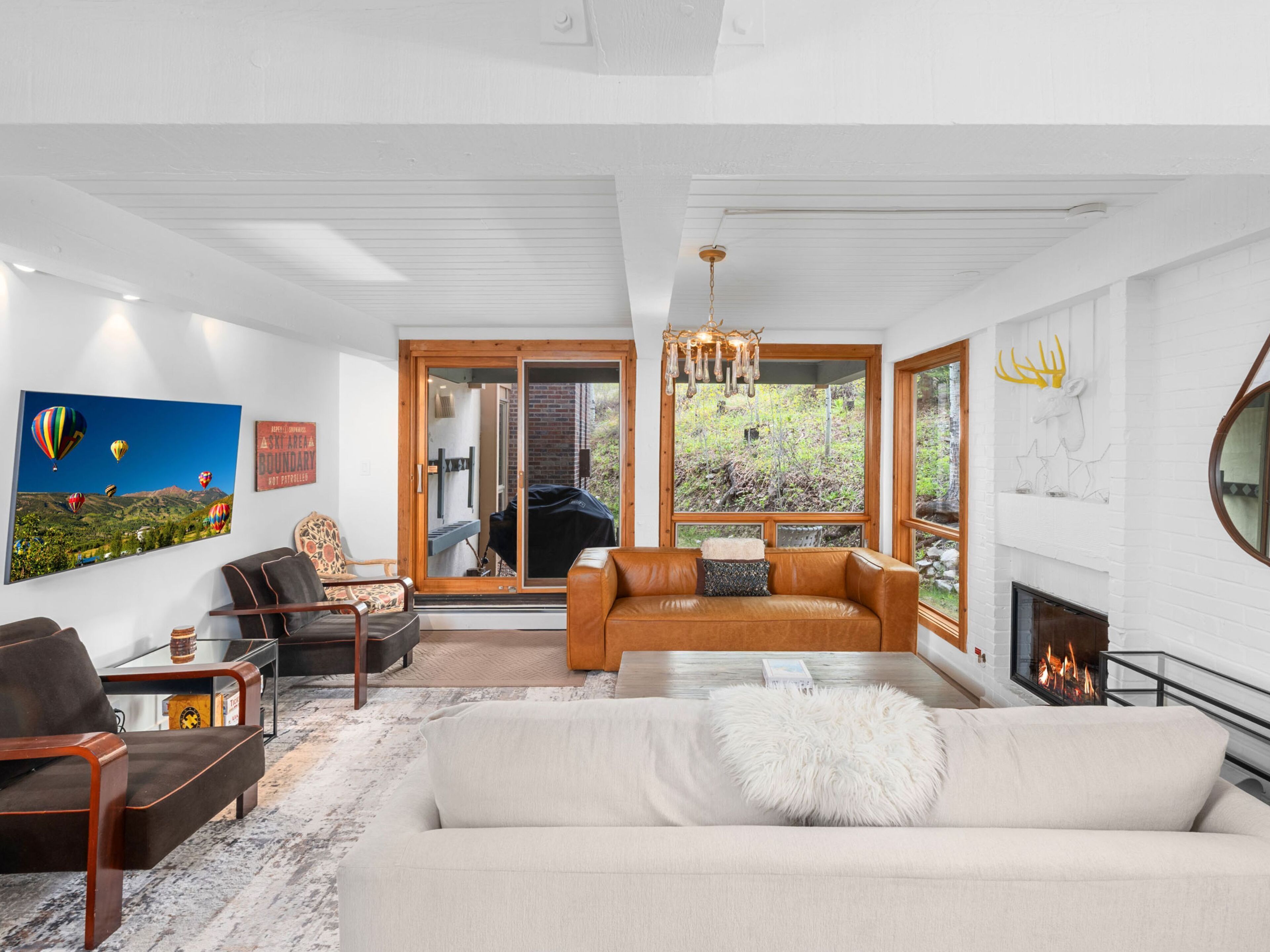 A modern living room with a fireplace, a large window with a view of greenery, and a cozy seating area.
