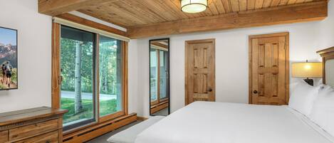 Une chambre dotée d’un grand lit, de poutres apparentes en bois au plafond, d’une commode en bois et d’une porte-fenêtre coulissante donnant sur un balcon.