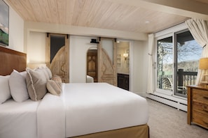 A bedroom with a large bed, wooden headboard, and a sliding glass door leading to a balcony. - Top of the Village (Snowmass Village)