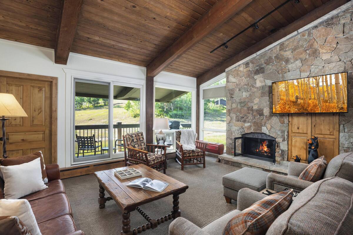 A cozy living room with a stone fireplace, wooden ceiling, and comfortable seating.