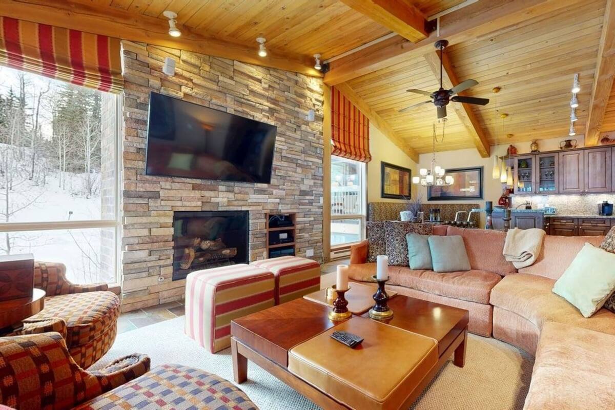 A cozy living room with a stone fireplace, a flat-screen TV, and a ceiling fan.