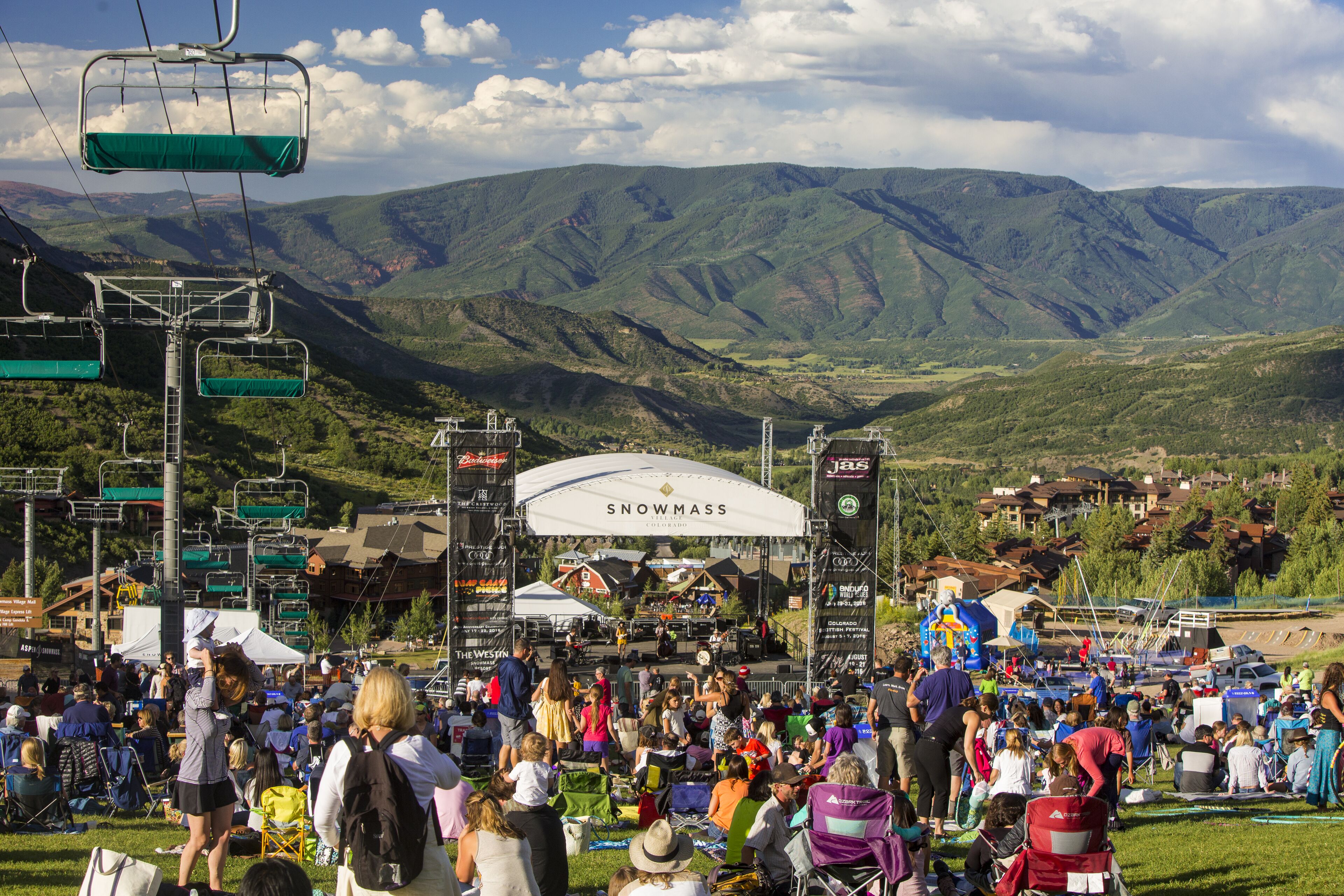 A crowded outdoor event with a stage and mountains in the background.
