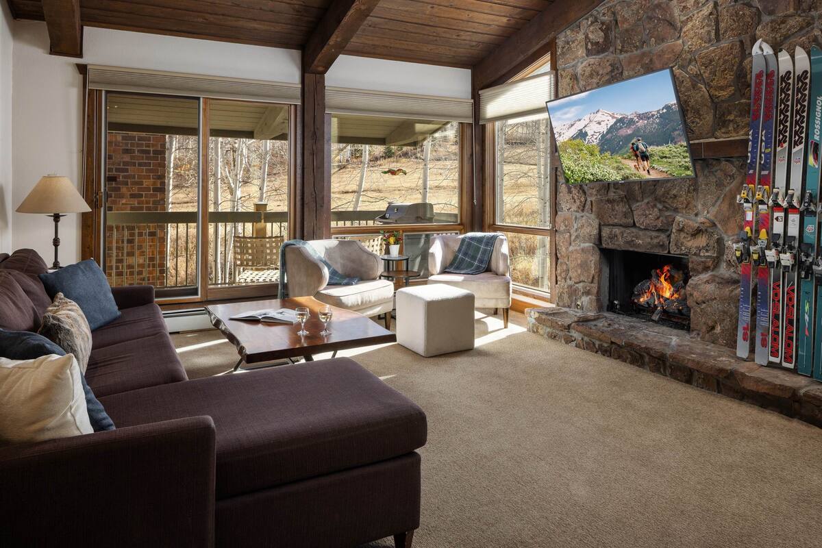 A cozy living room with a stone fireplace, a large TV, and a ski rack.