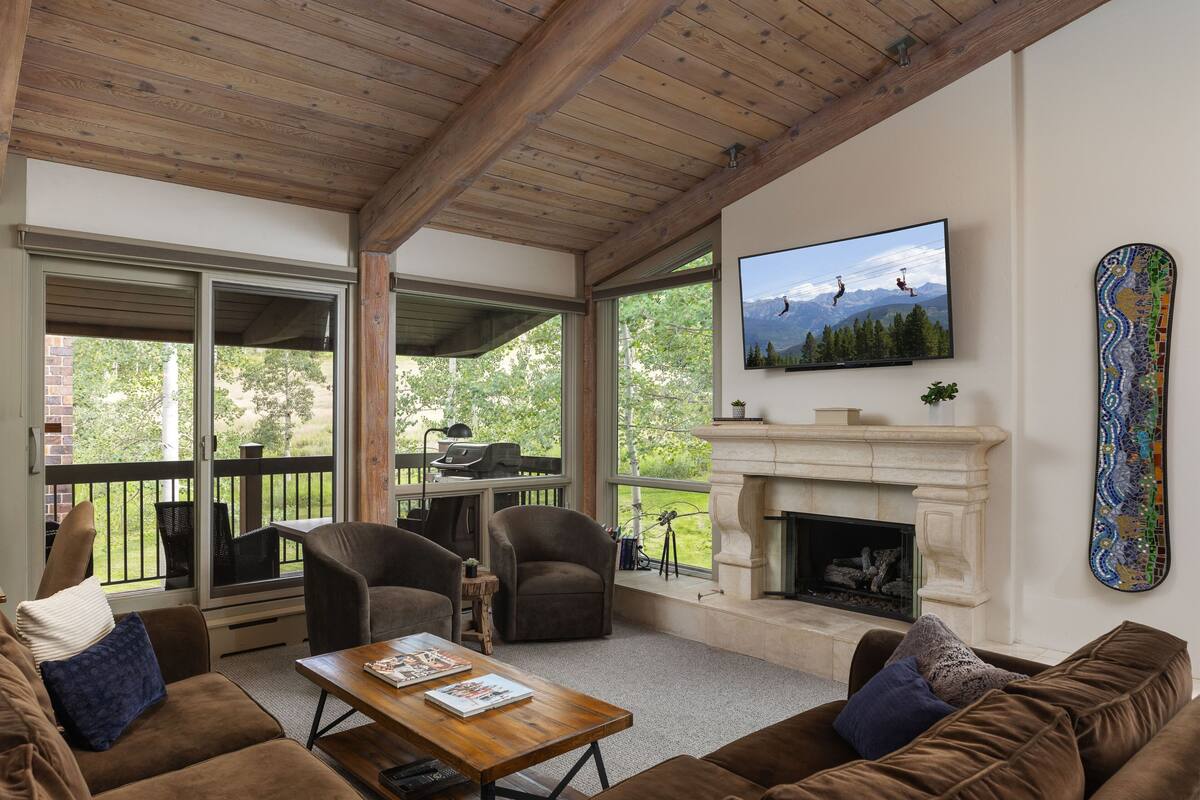 A cozy living room with a fireplace, comfortable seating, a television, and a balcony with a grill.