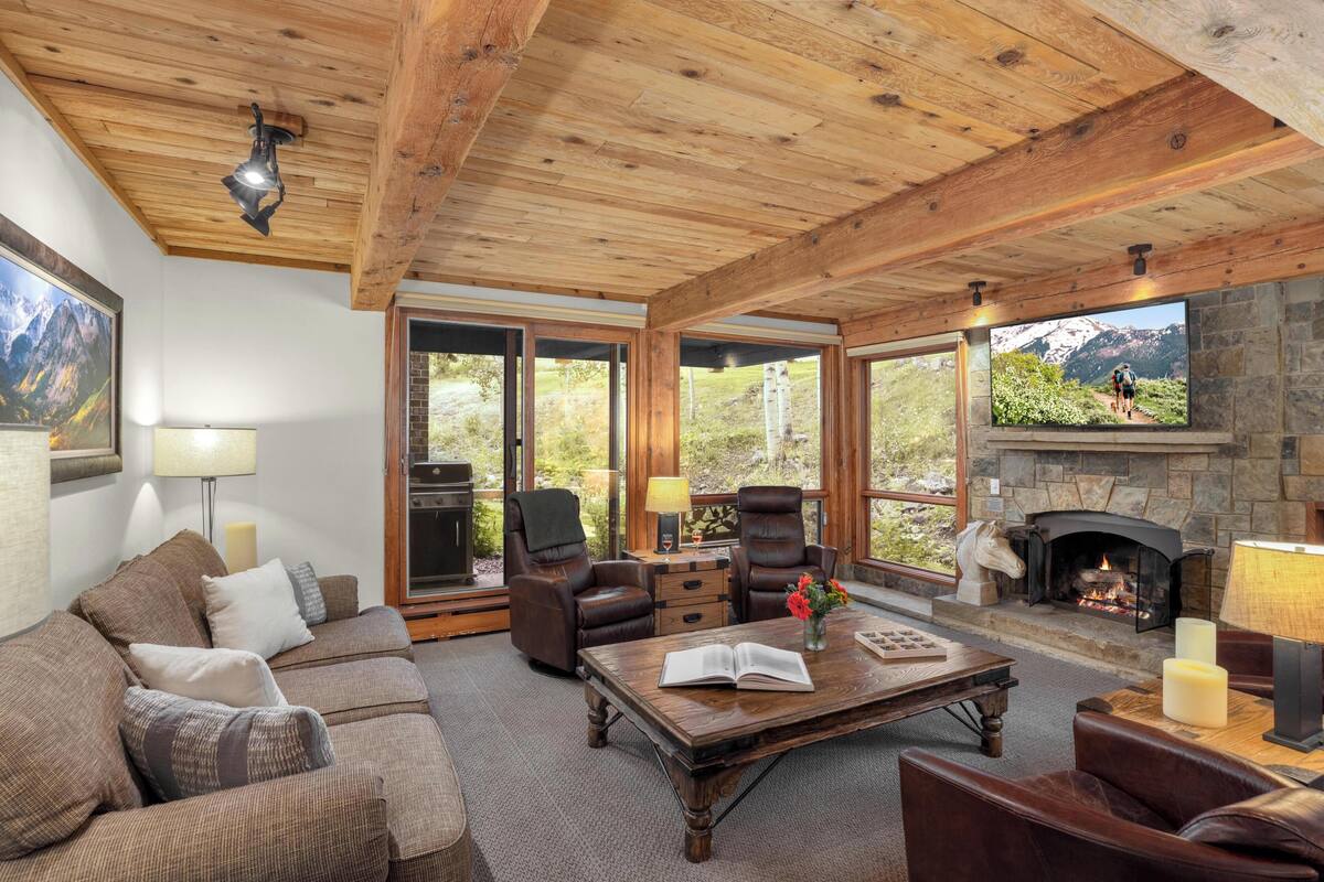 A cozy living room with a fireplace, leather furniture, and large windows offering mountain views.