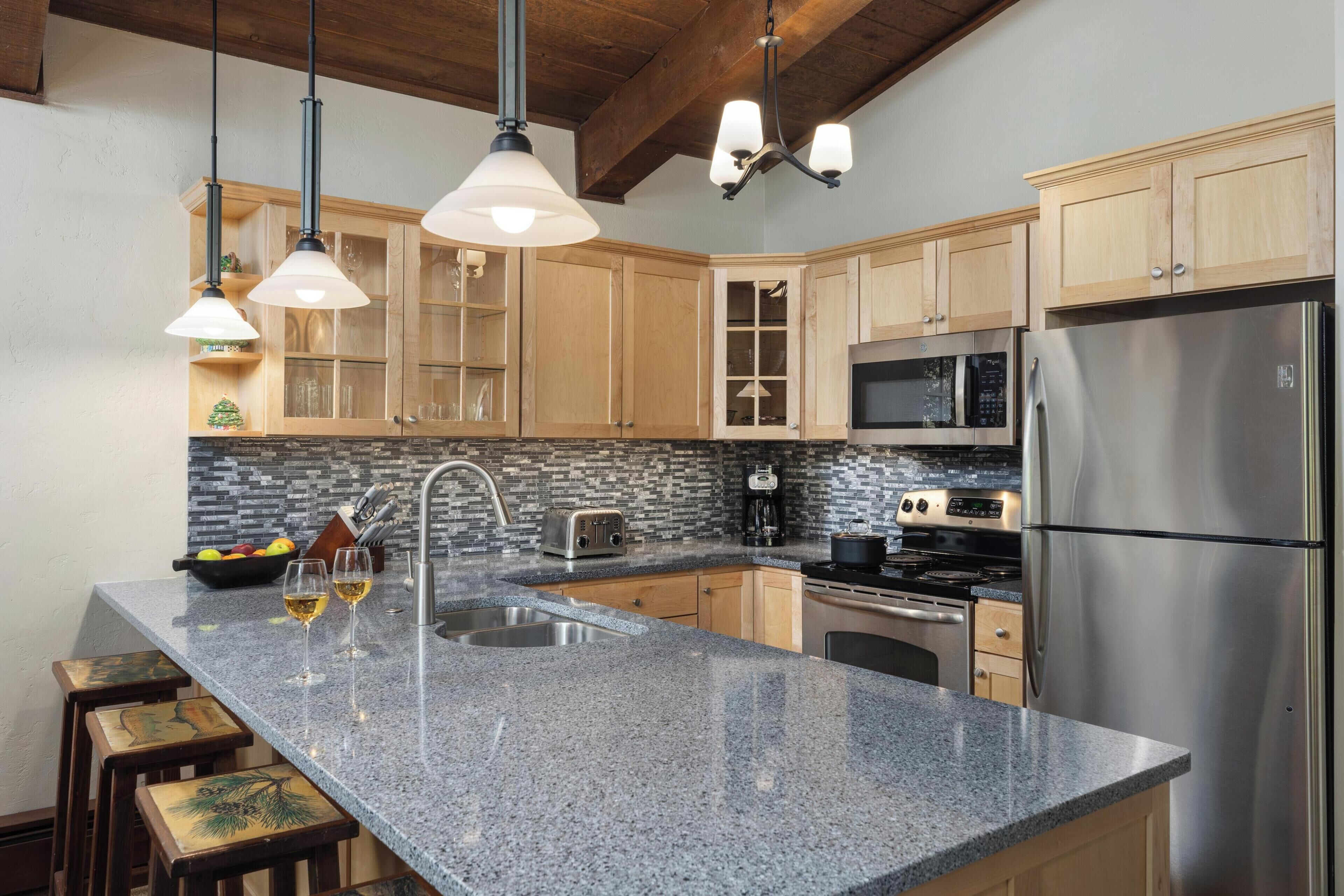 A kitchen with granite countertops, wooden cabinets, stainless steel appliances, and pendant lighting.