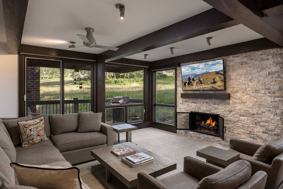A modern living room with a fireplace, large windows, and a stone wall.