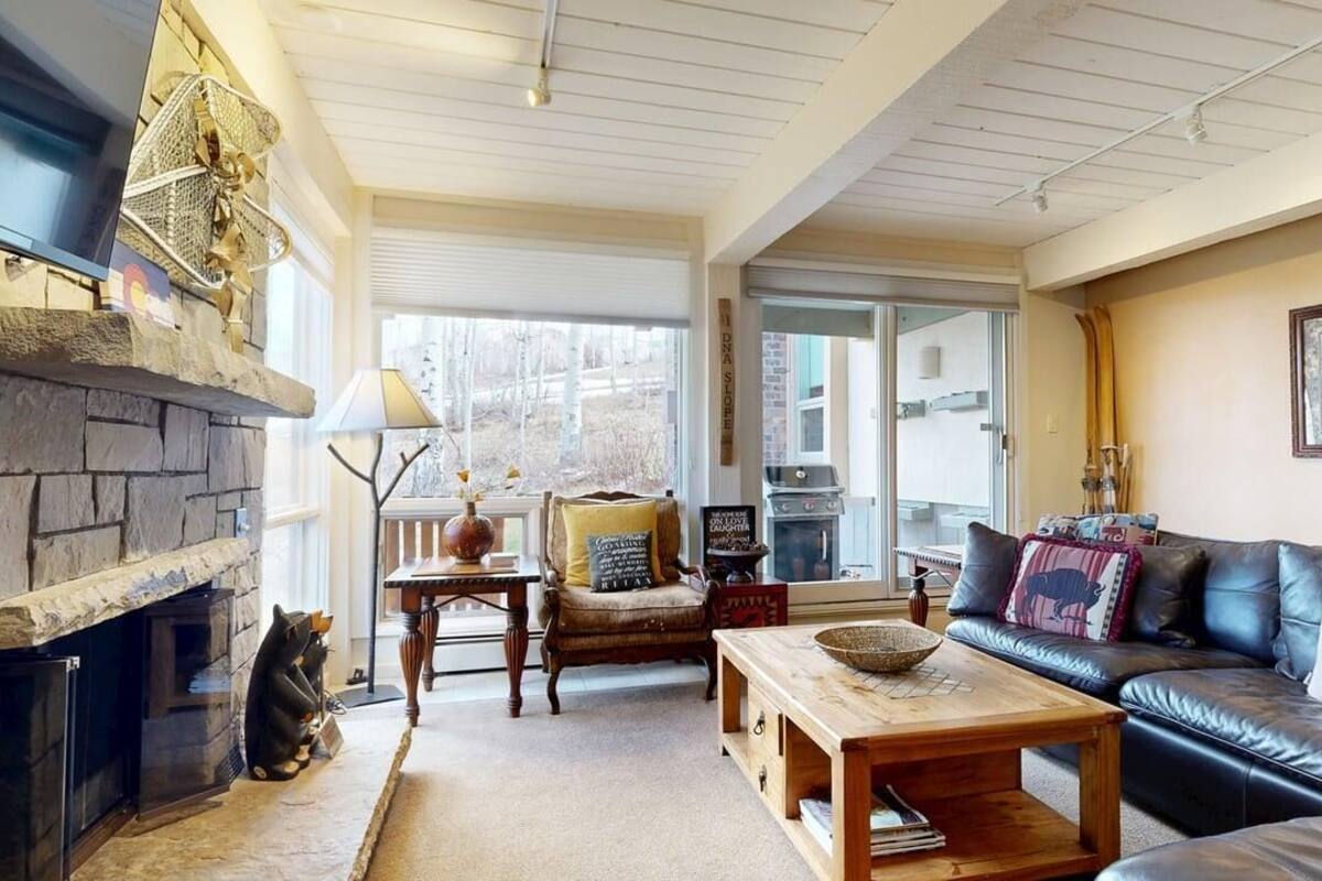A cozy living room with a stone fireplace, leather sofa, wooden coffee table, and a comfortable chair.