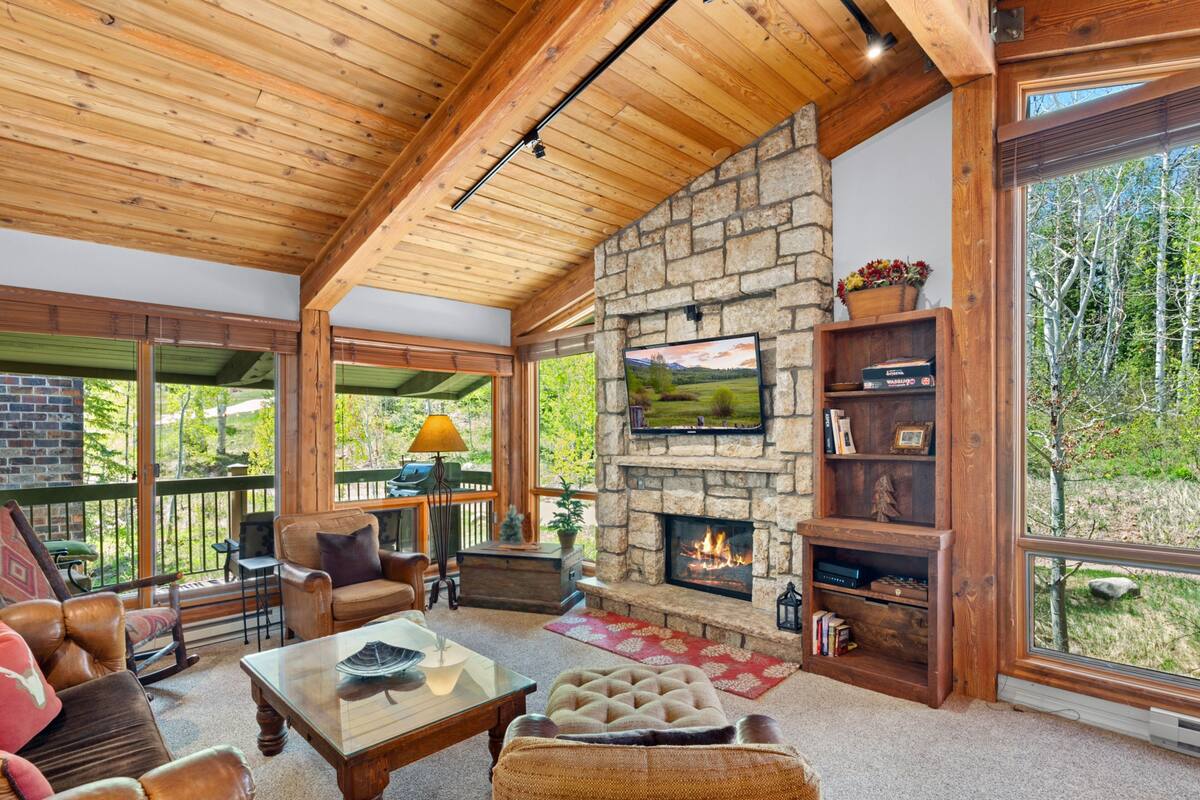 A cozy living room with a stone fireplace, leather furniture, and a large TV mounted on the wall.