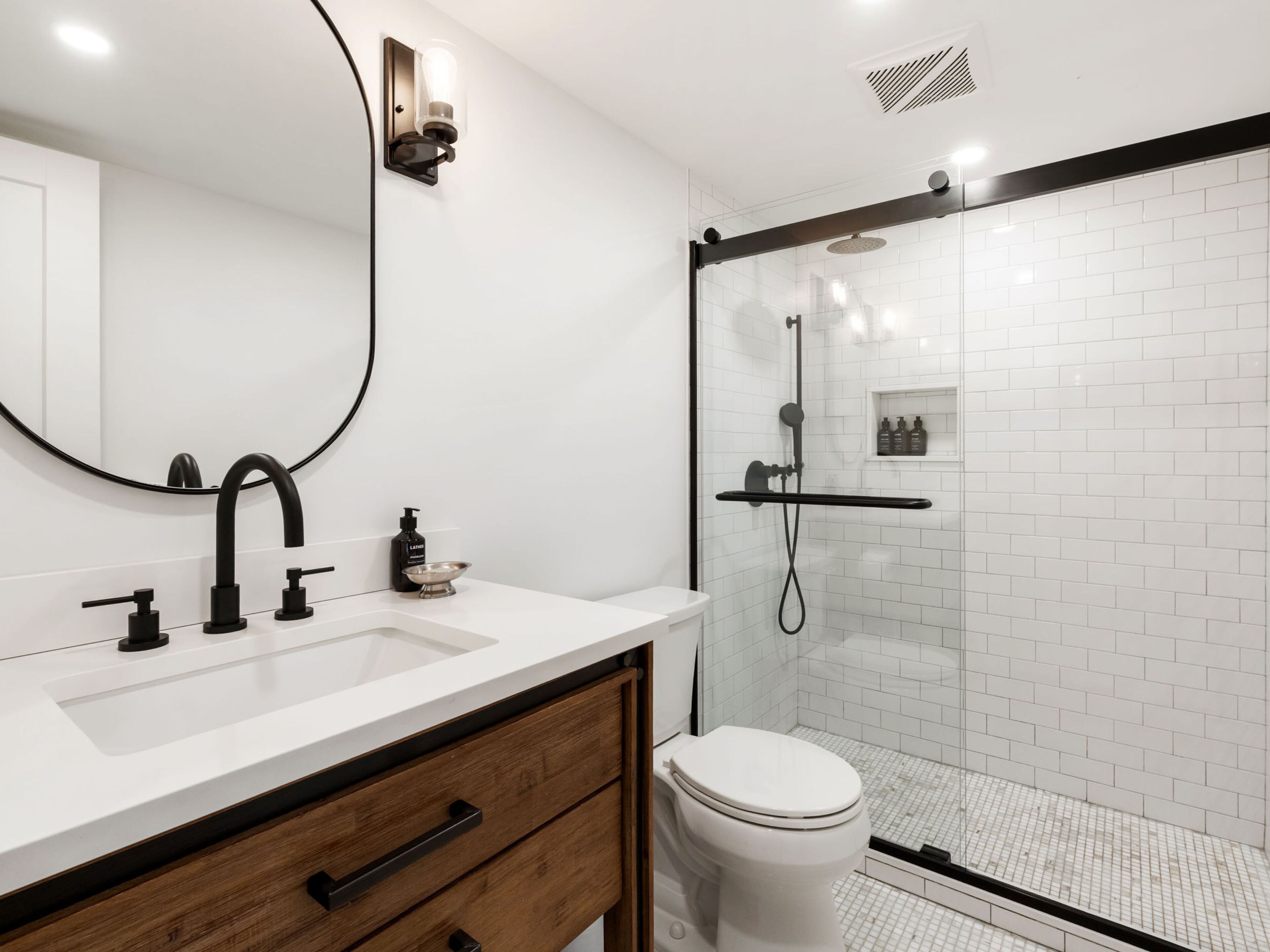 A modern bathroom with a white sink, black faucet, and a glass-enclosed shower area.