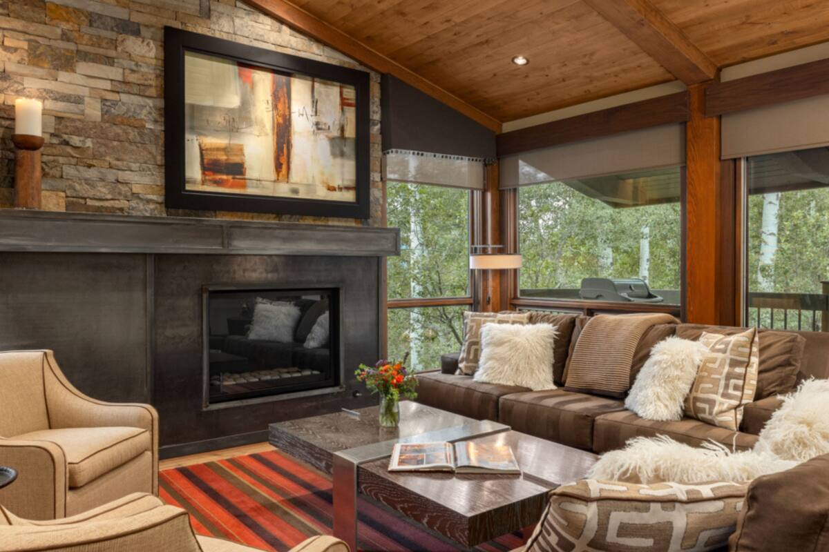 A modern living room with a stone fireplace, comfortable seating, and large windows offering a view of the outdoors.