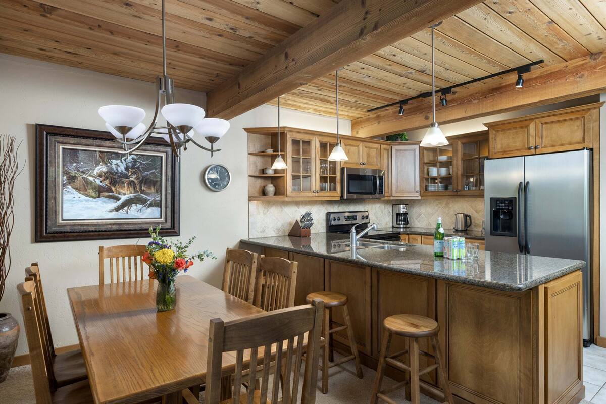 A kitchen with wooden cabinets, a stainless steel refrigerator, and a dining area with a wooden table and chairs.