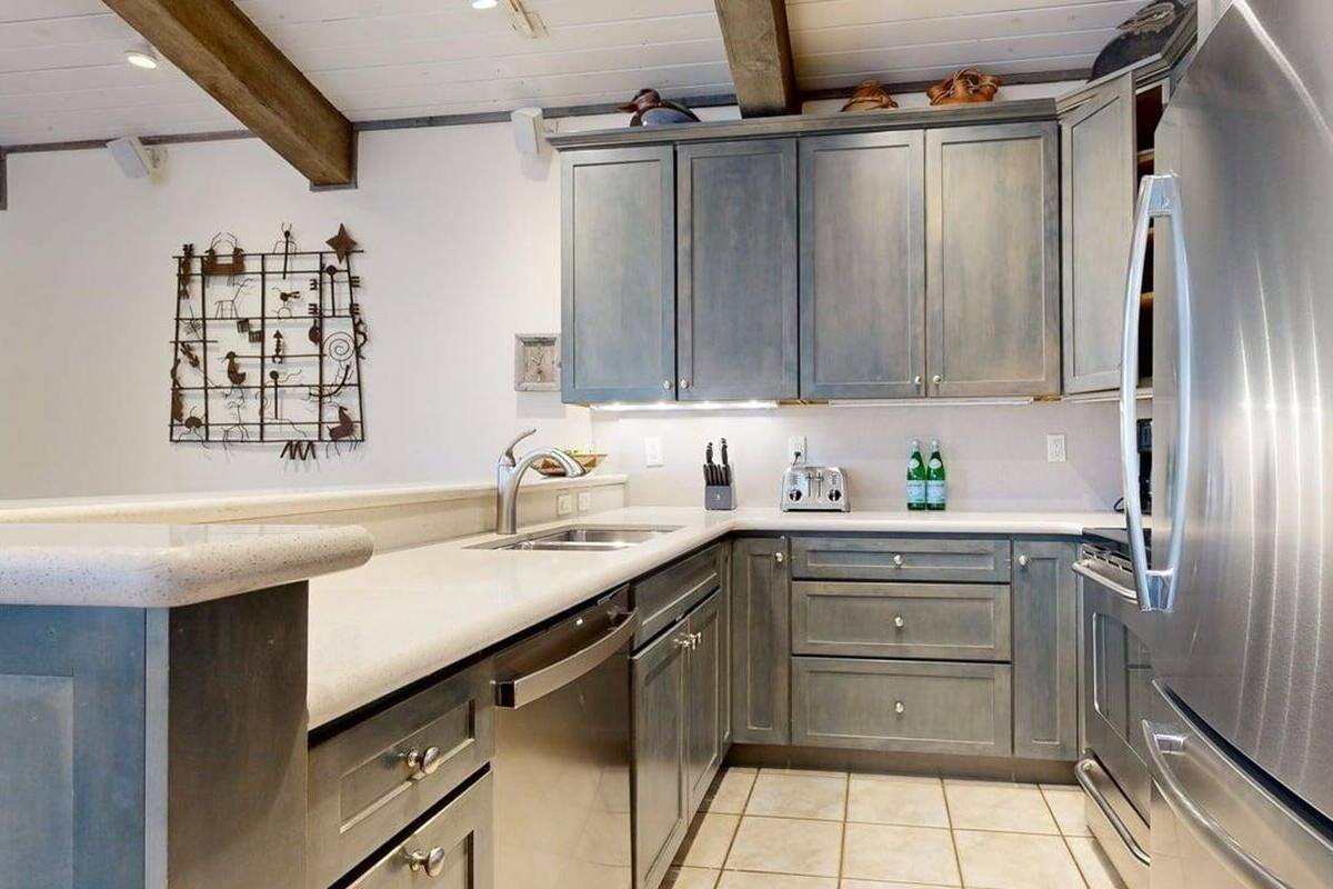 A kitchen with grey cabinets, a stainless steel refrigerator, a sink, and a decorative wall piece.