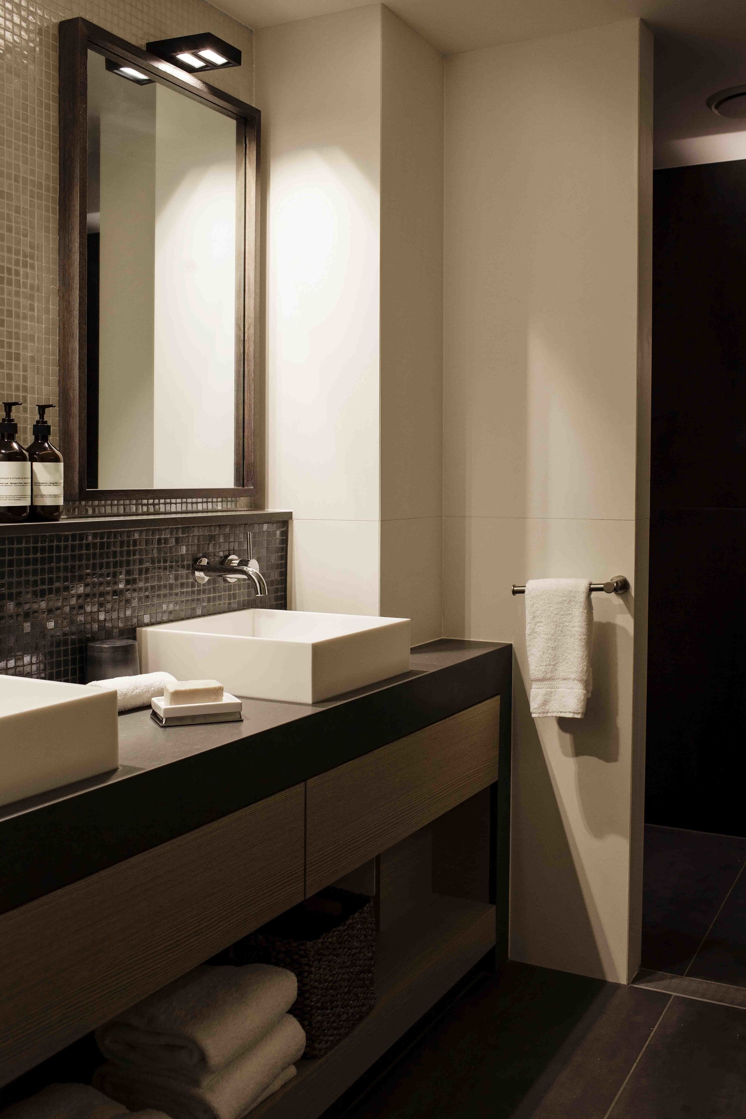 A modern bathroom with two sinks, a large mirror, and a towel rack.