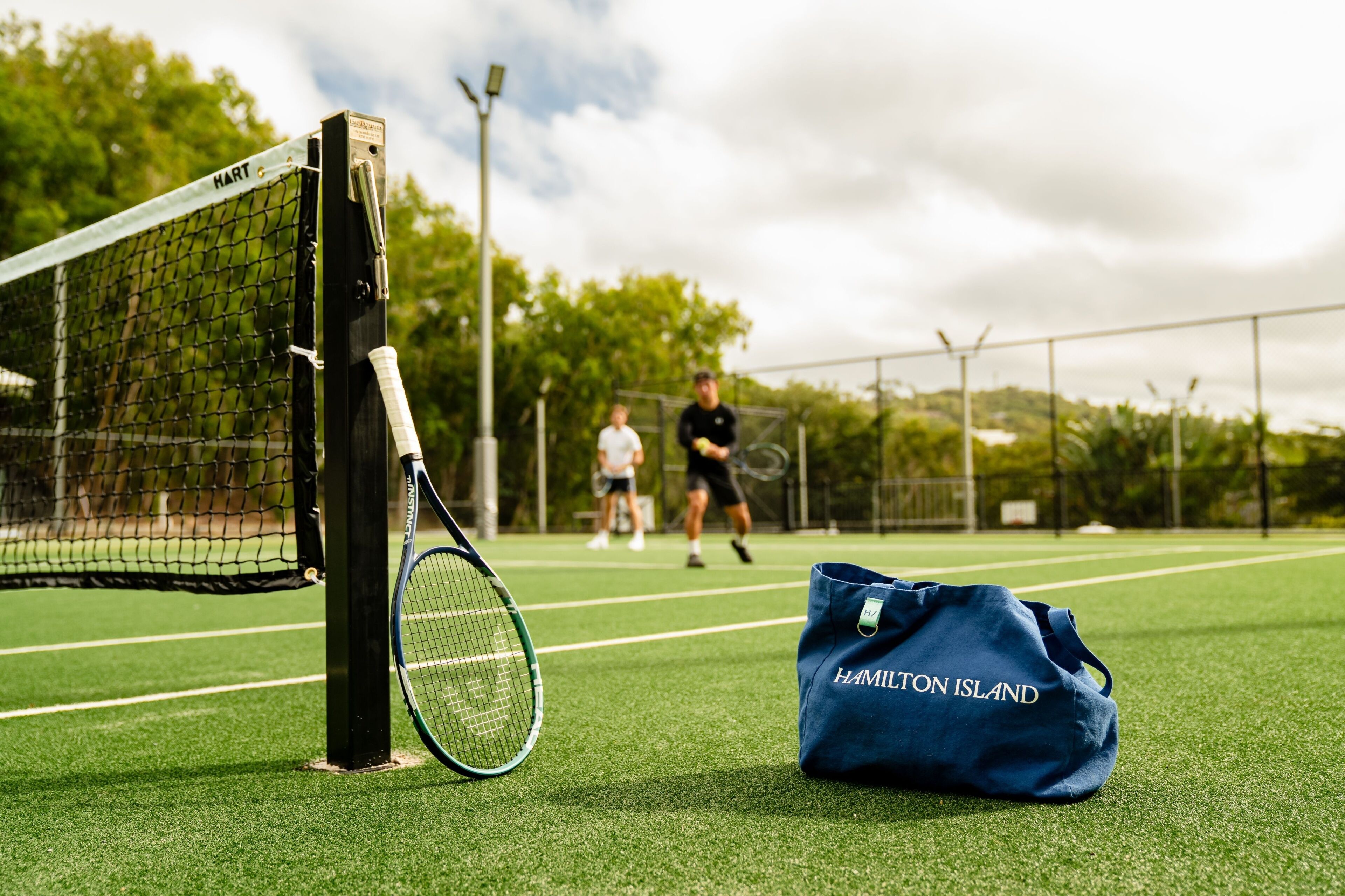 Un court de tennis avec un filet, une raquette de tennis et un sac sur lequel on peut lire « HAMILTON ISLAND ».