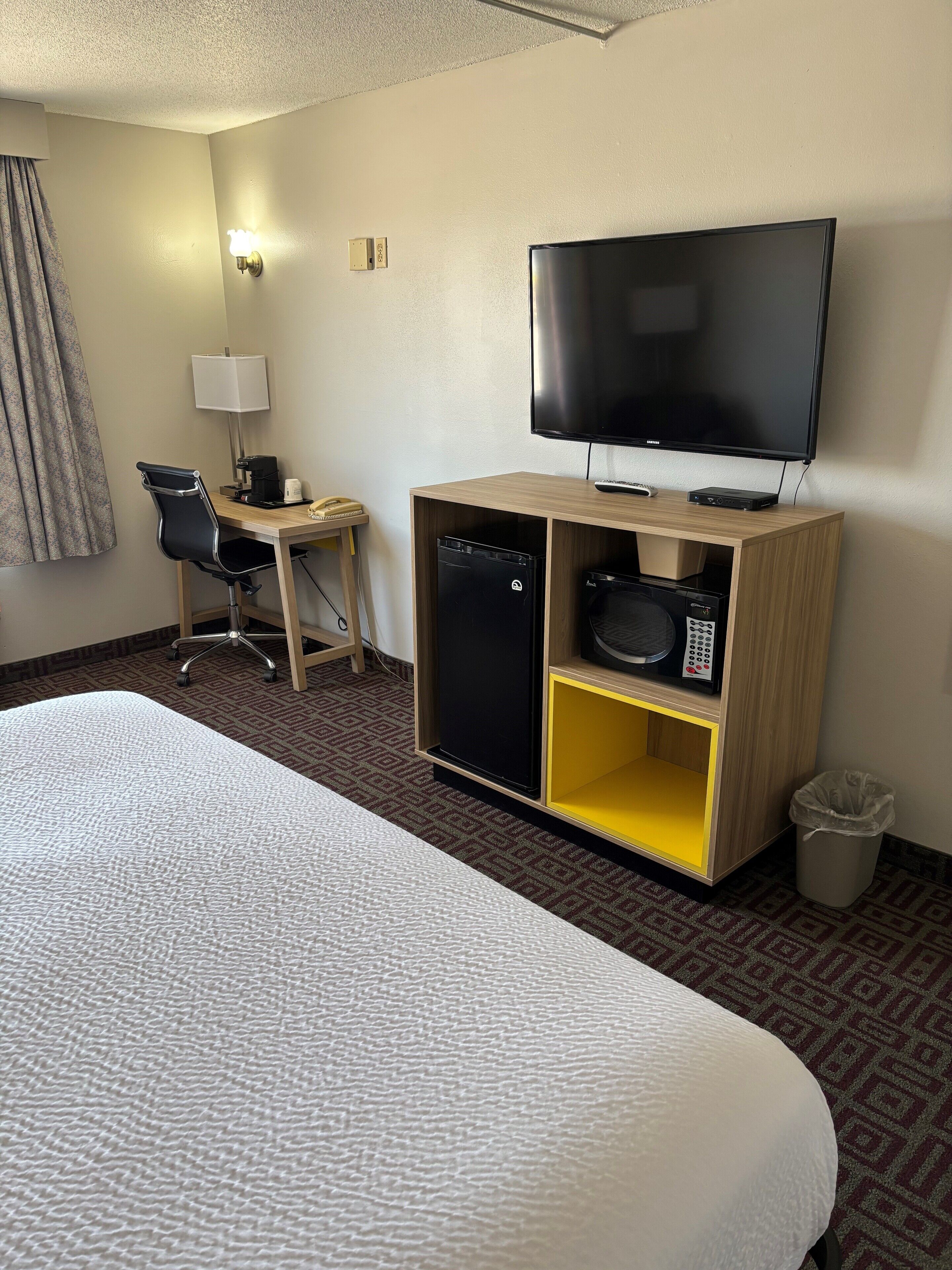 Ein Hotelzimmer mit Bett, Schreibtisch mit Lampe, Fernseher, Mikrowelle und Mülleimer.