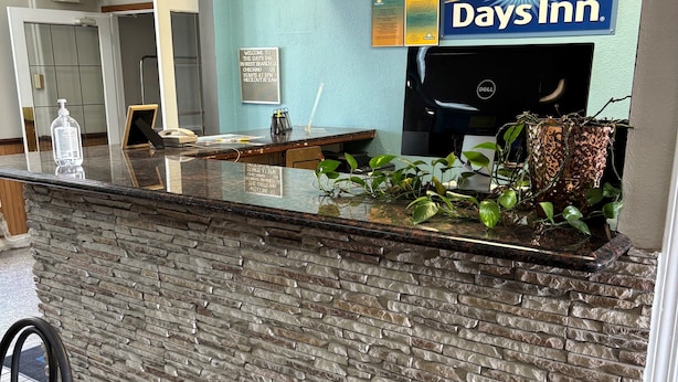 Una zona de recepción con el letrero de Days Inn, un mostrador de textura de piedra, una computadora Dell y una planta en maceta.