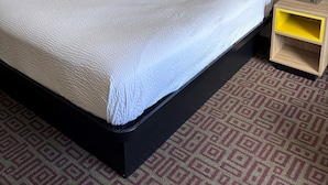 Una habitación de hotel con una cama grande, dos lámparas de noche, un cuadro con un árbol y una alfombra estampada.