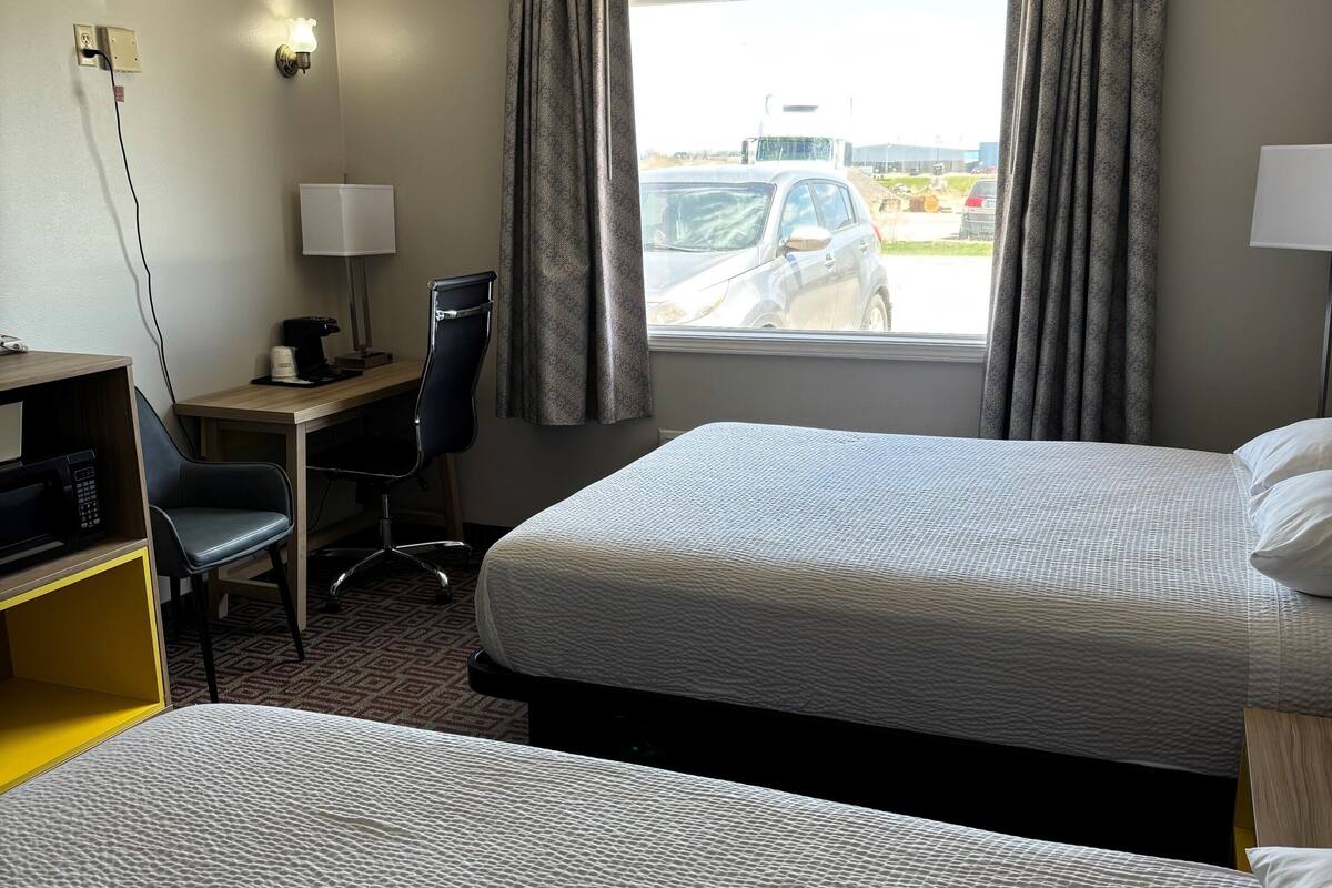 A hotel room with two beds, a desk, a chair, and a window with curtains.