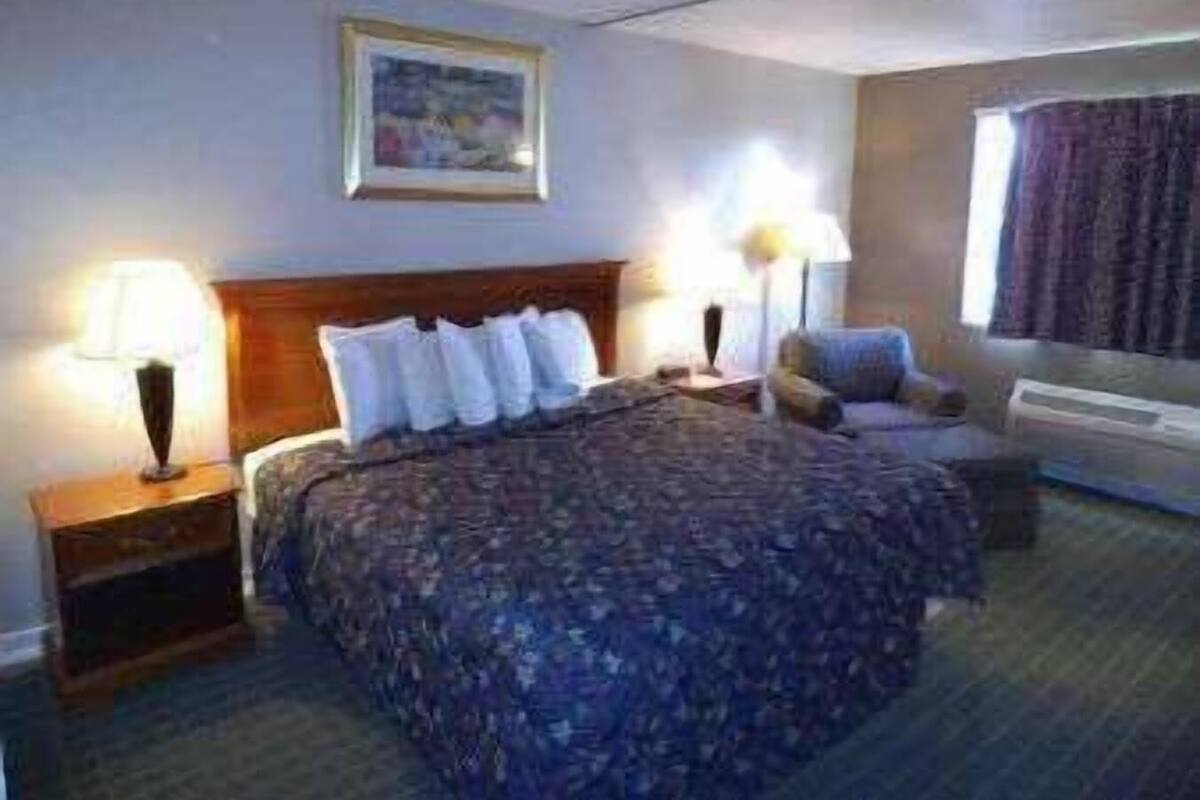 A hotel room with a bed, bedside lamps, a chair, and a painting on the wall.
