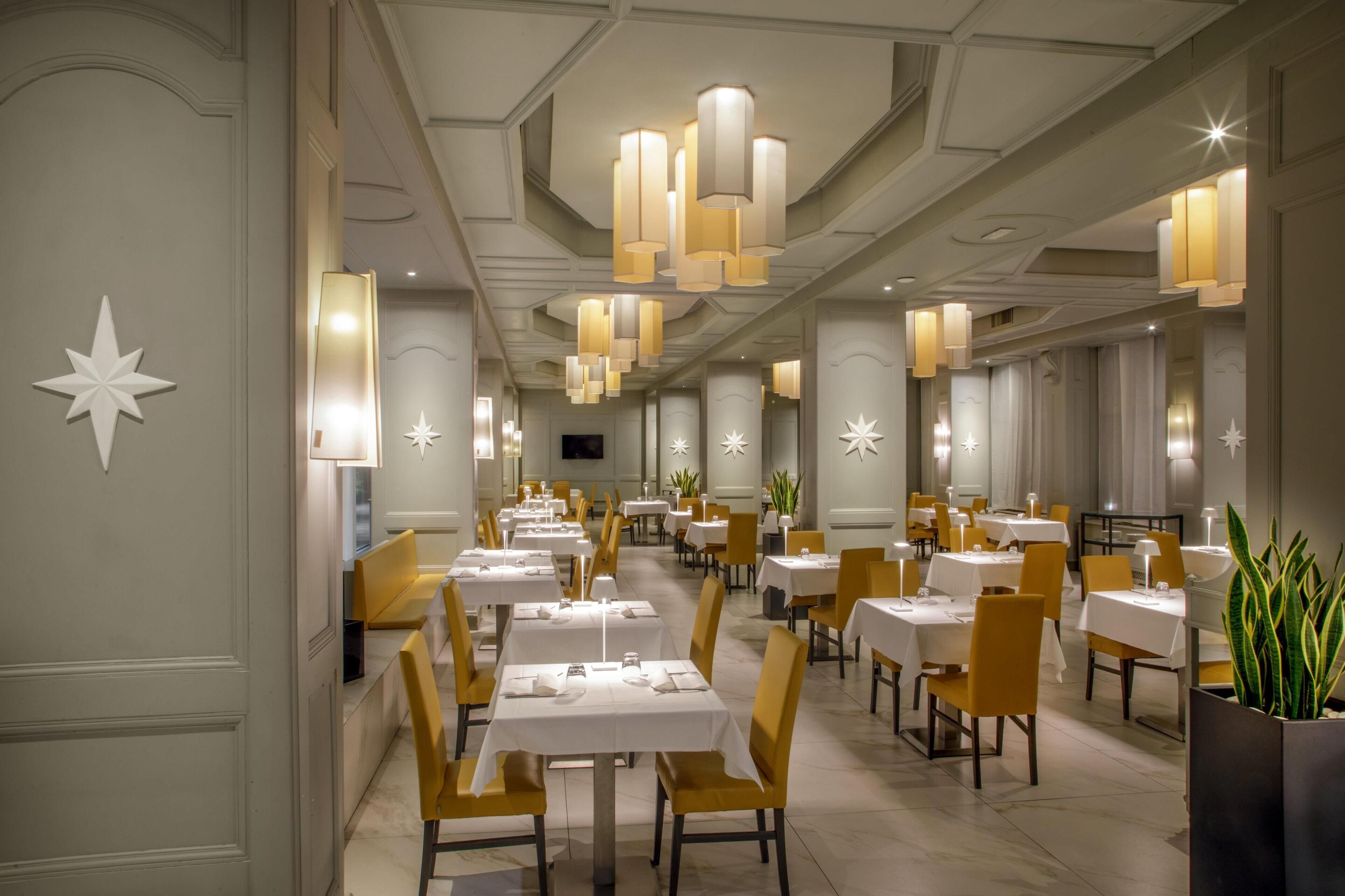 Un vaste espace dédié à la salle à manger, avec de nombreuses tables et chaises, un éclairage d’ambiance et des motifs décoratifs en forme d’étoiles sur les murs.
