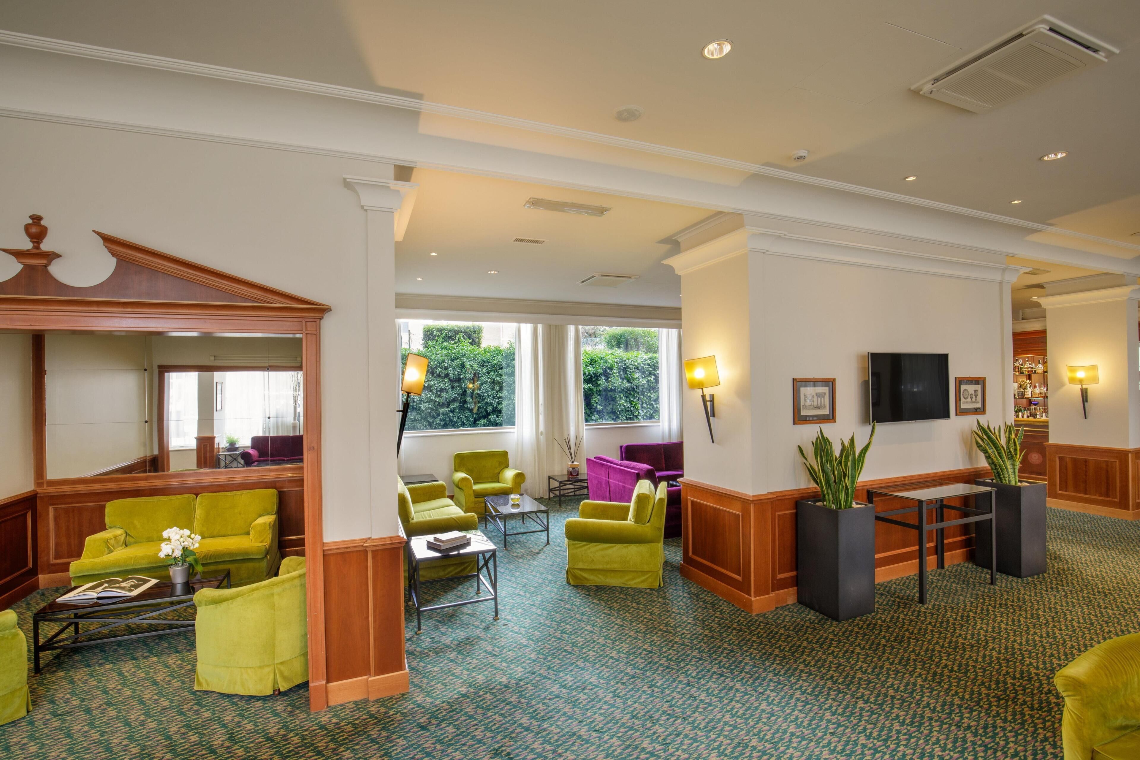 A hotel lobby with green upholstered seating, a reception desk, and large windows.