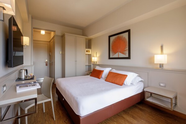 A hotel room with a bed, desk, chair, and a television.