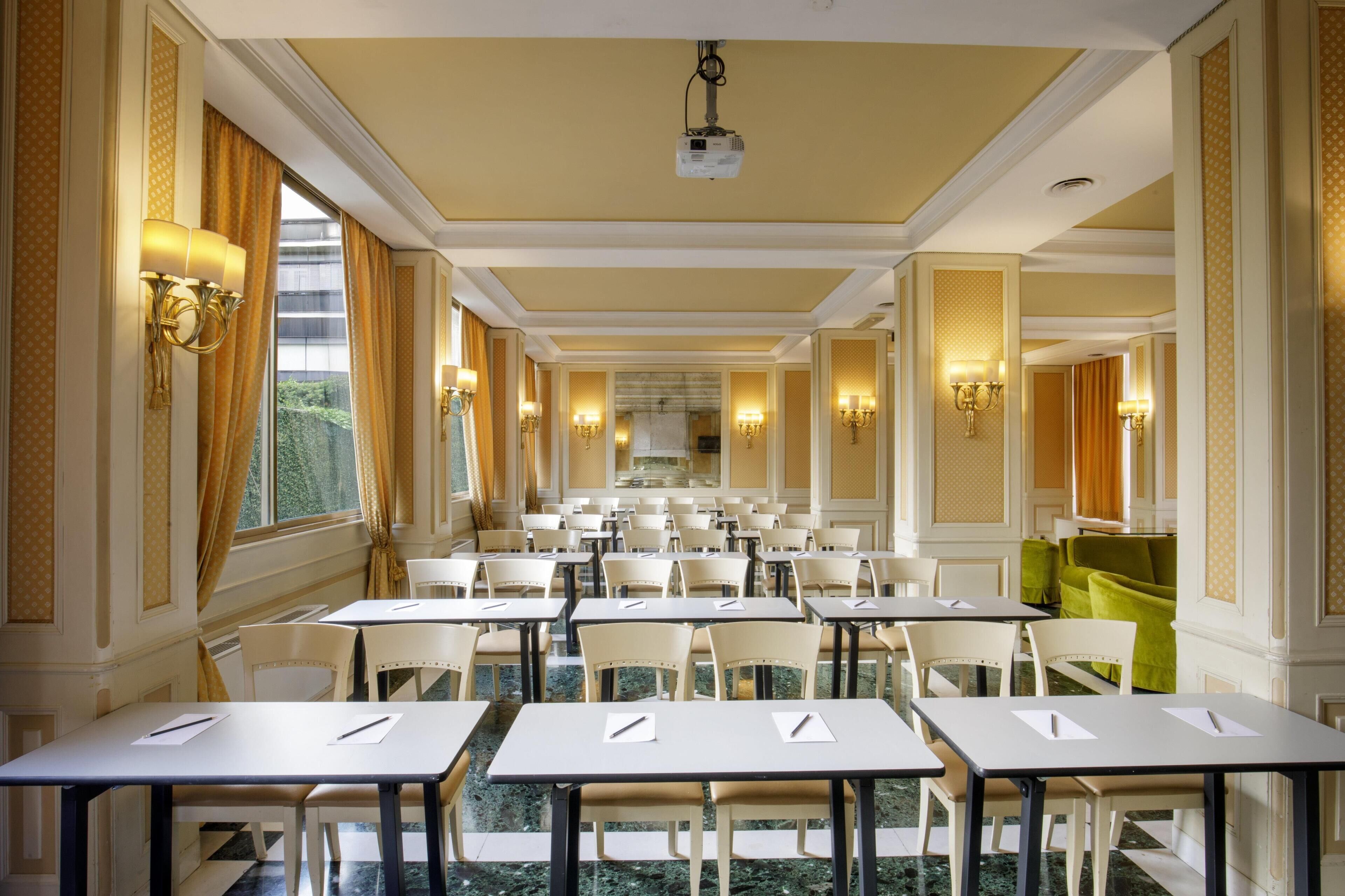 Un comedor de hotel con mesas y sillas, candelabros y un proyector en el techo.