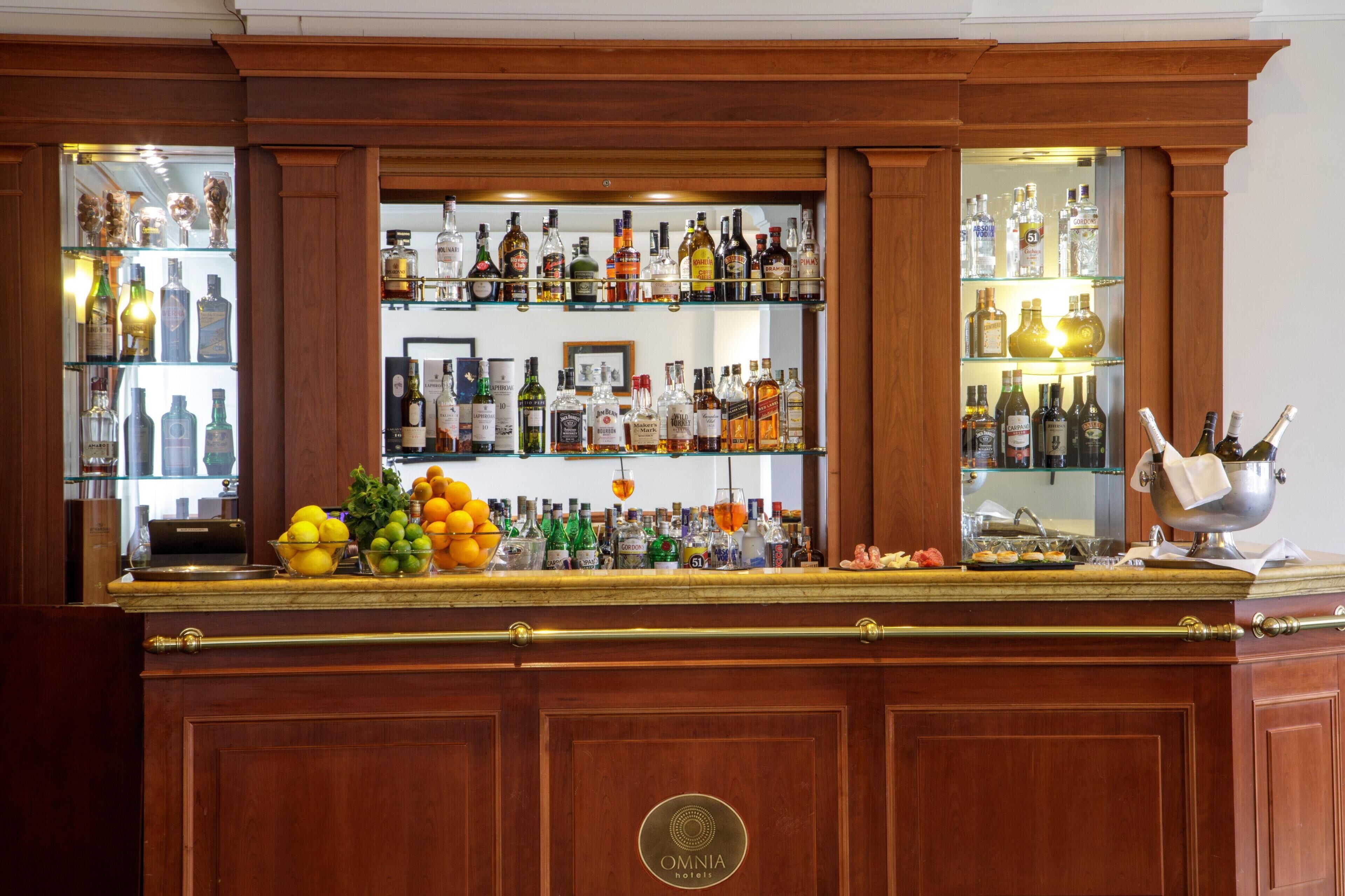 Un bar doté de plusieurs étagères remplies de bouteilles d’alcool, d’un panier de fruits et d’un vase décoratif recouvert d’un tissu.