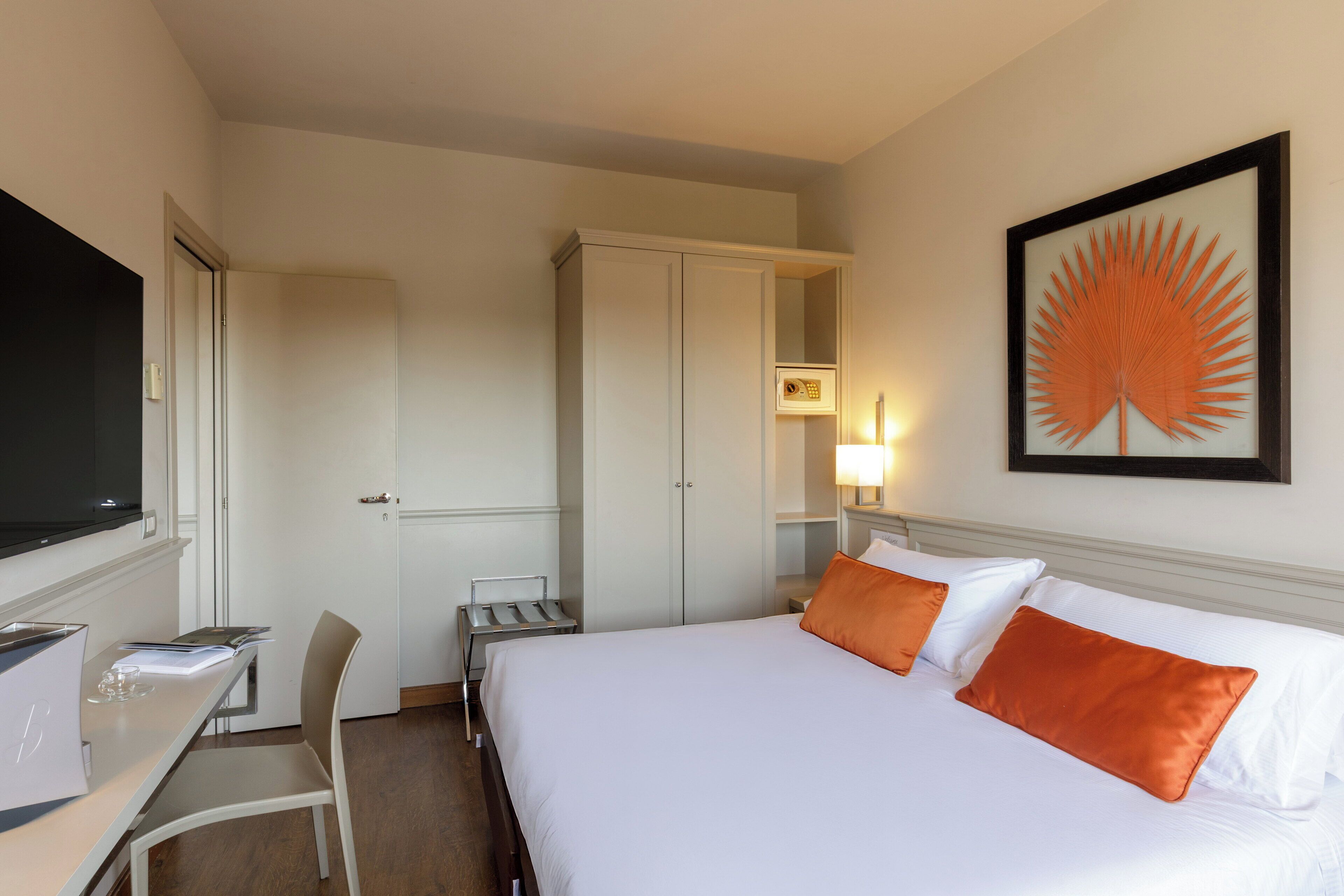 Habitación de hotel con cama, escritorio, silla, televisión y un cuadro en la pared.