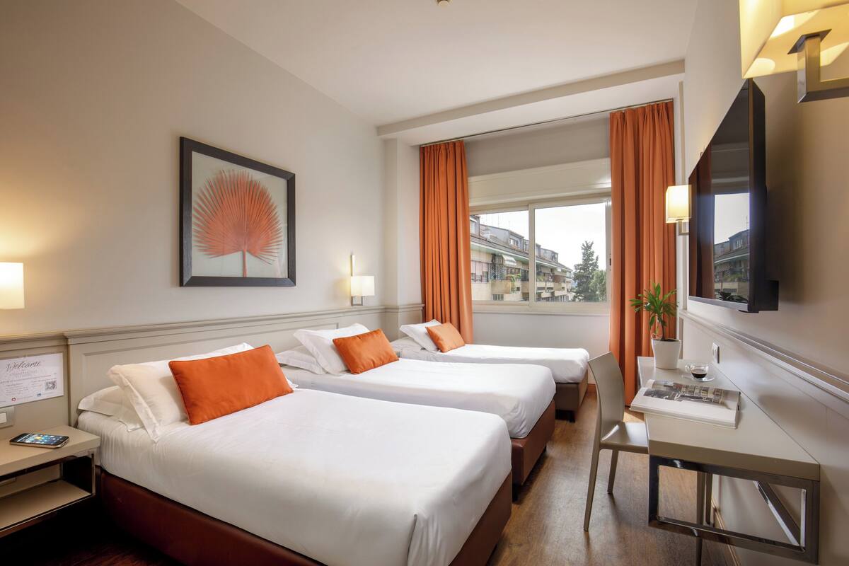 A hotel room with two beds, a desk, a TV, and a window with curtains.