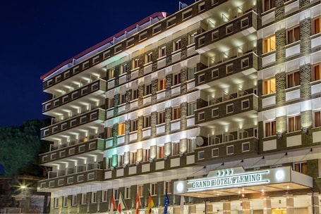 A multi-story hotel with balconies, a sign reading 'Grand Hotel Fleming,' and multiple flags.