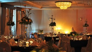 Een balzaal met gedekte tafels voor een formeel evenement, versierd met bloemstukken en verlicht door een kroonluchter.