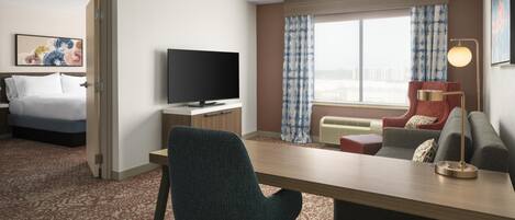 Habitación de hotel con cama, escritorio con silla, televisor, sofá y ventana con cortinas.