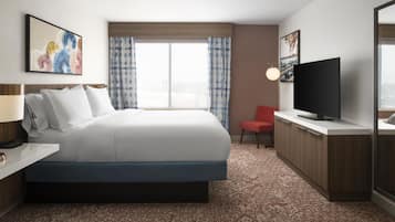A hotel room with a large bed, a flat-screen TV, a desk with a lamp, and a red chair.