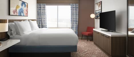 A hotel room with a large bed, a flat-screen TV, a desk with a lamp, and a red chair.