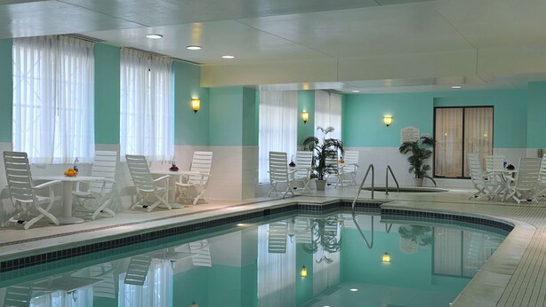 Een zwembad met witte stoelen en een tafel, omringd door turquoise muren en witte gordijnen.