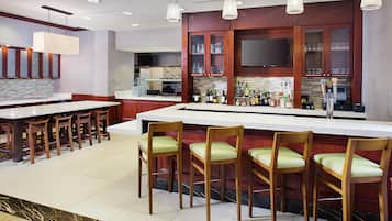 A modern kitchen with a bar area, wooden chairs, and a flat-screen TV above the counter.