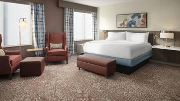 A hotel room with a large bed, a chair, a small table, and a floor lamp.
