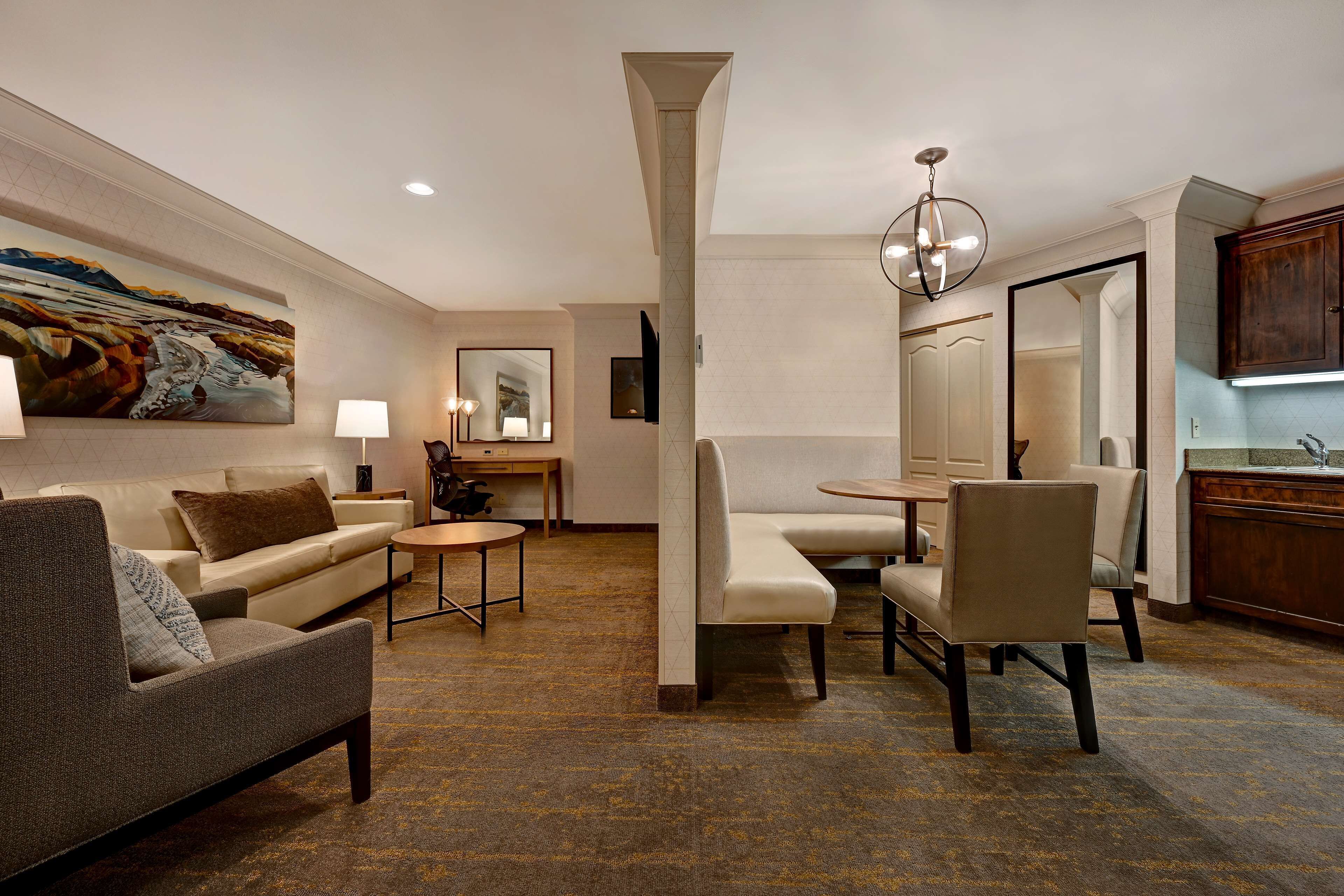 Une chambre d’hôtel moderne équipée d’un canapé, d’un fauteuil, d’une table à manger et d’un grand miroir.