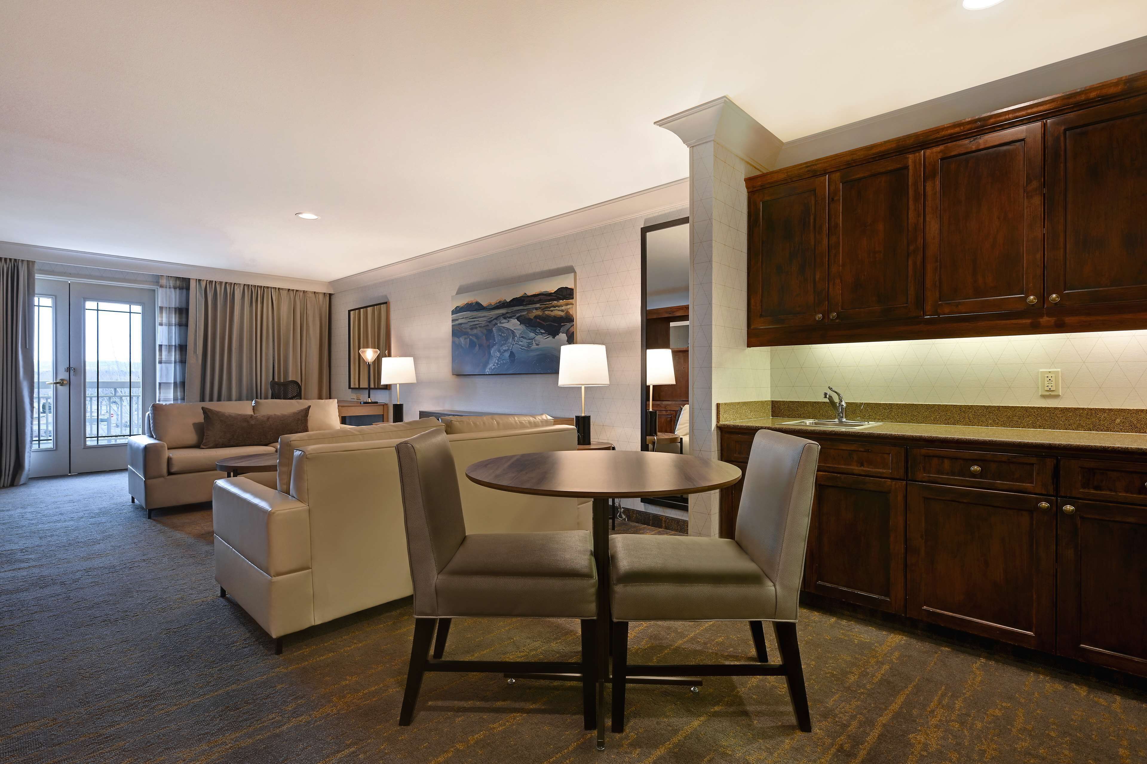 A modern hotel room with a dining area, a sofa set, a round table, and wooden cabinets.
