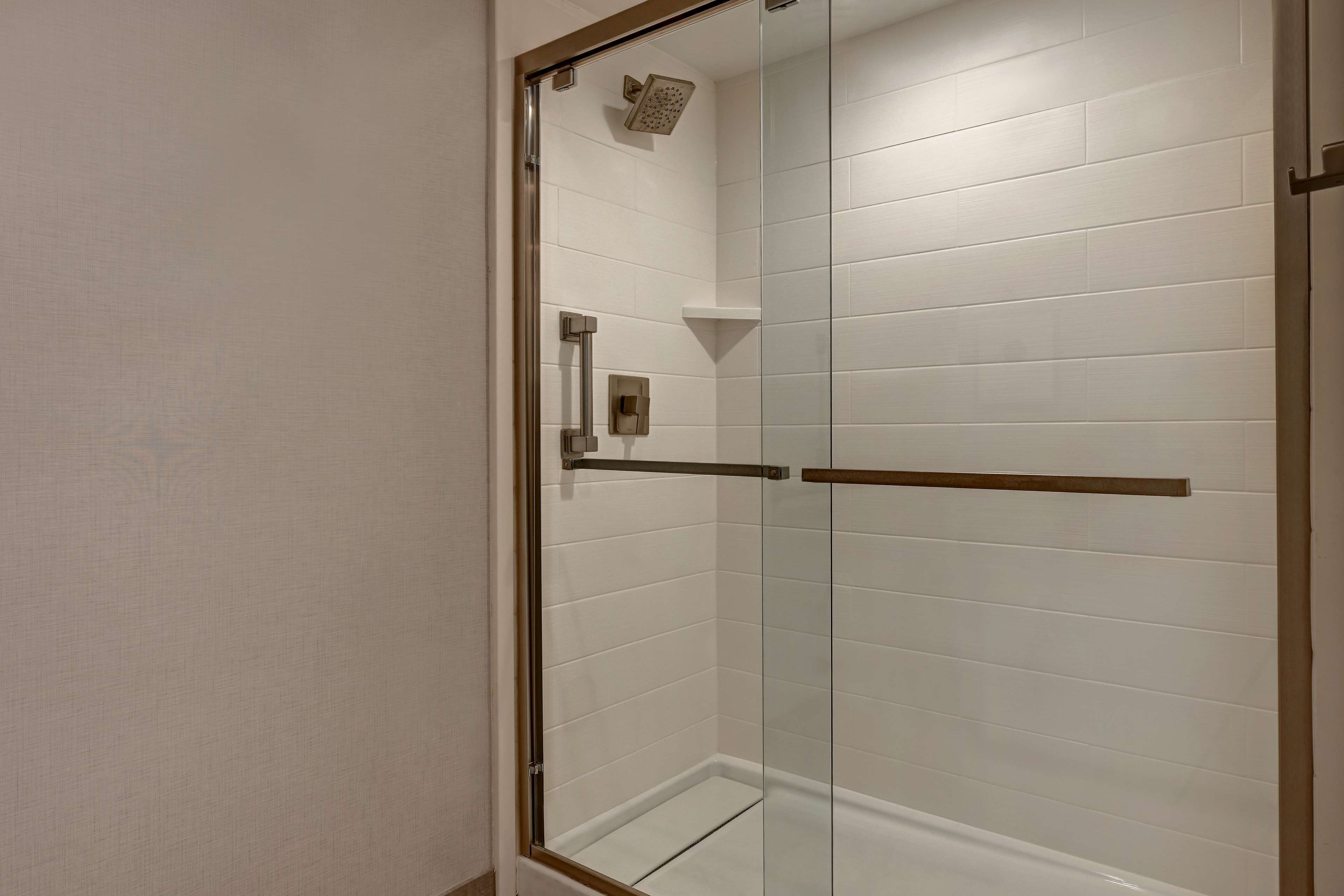 A glass-enclosed shower with white tiles, a handheld showerhead, and a towel bar.