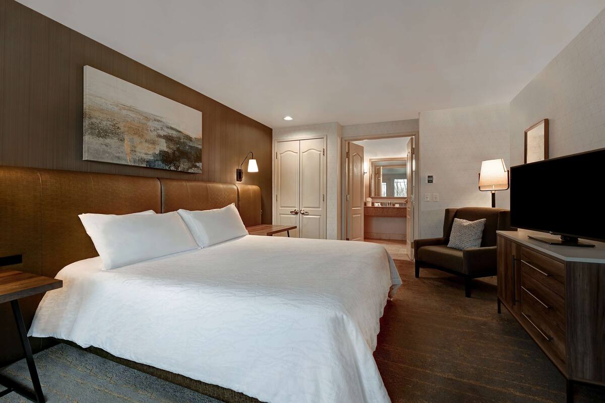 A hotel room with a large bed, a television, a desk, and a chair.